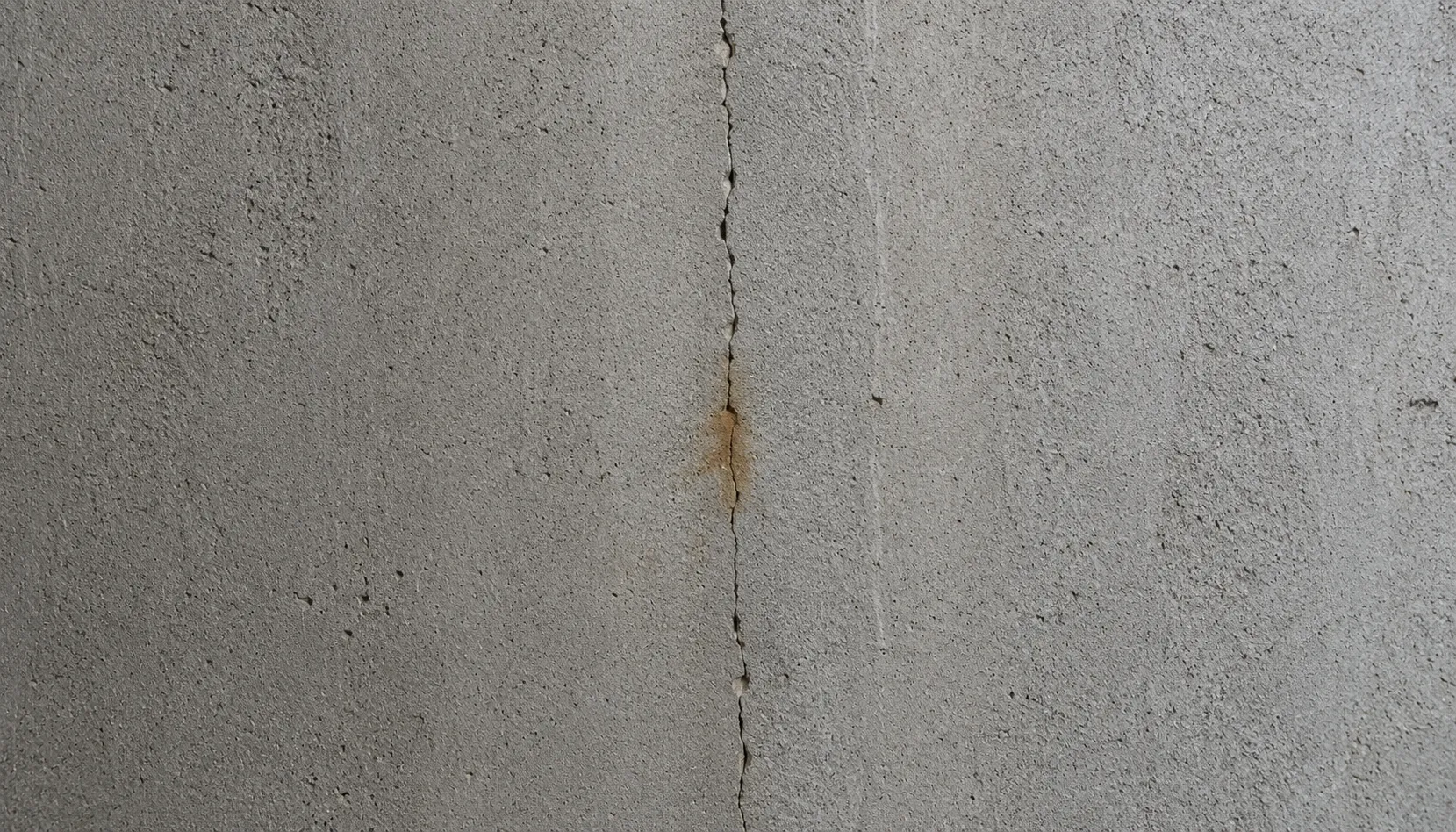 Vertical hairline crack running down a poured concrete basement foundation wall with a faint rust-coloured stain at the midpoint